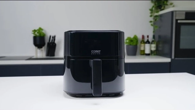 Black Caso Design air fryer on a white table in a kitchen setting.