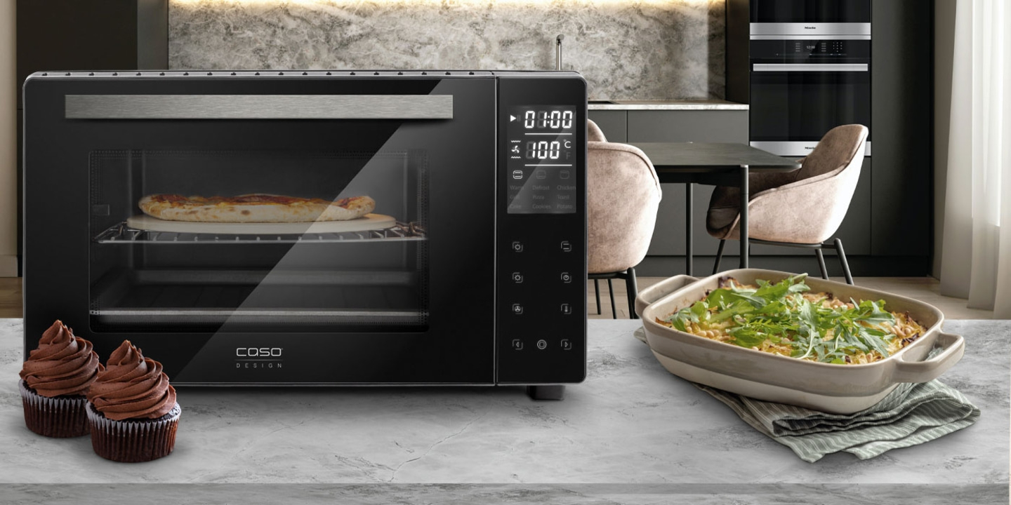 Black oven with pizza and cupcakes on a kitchen countertop