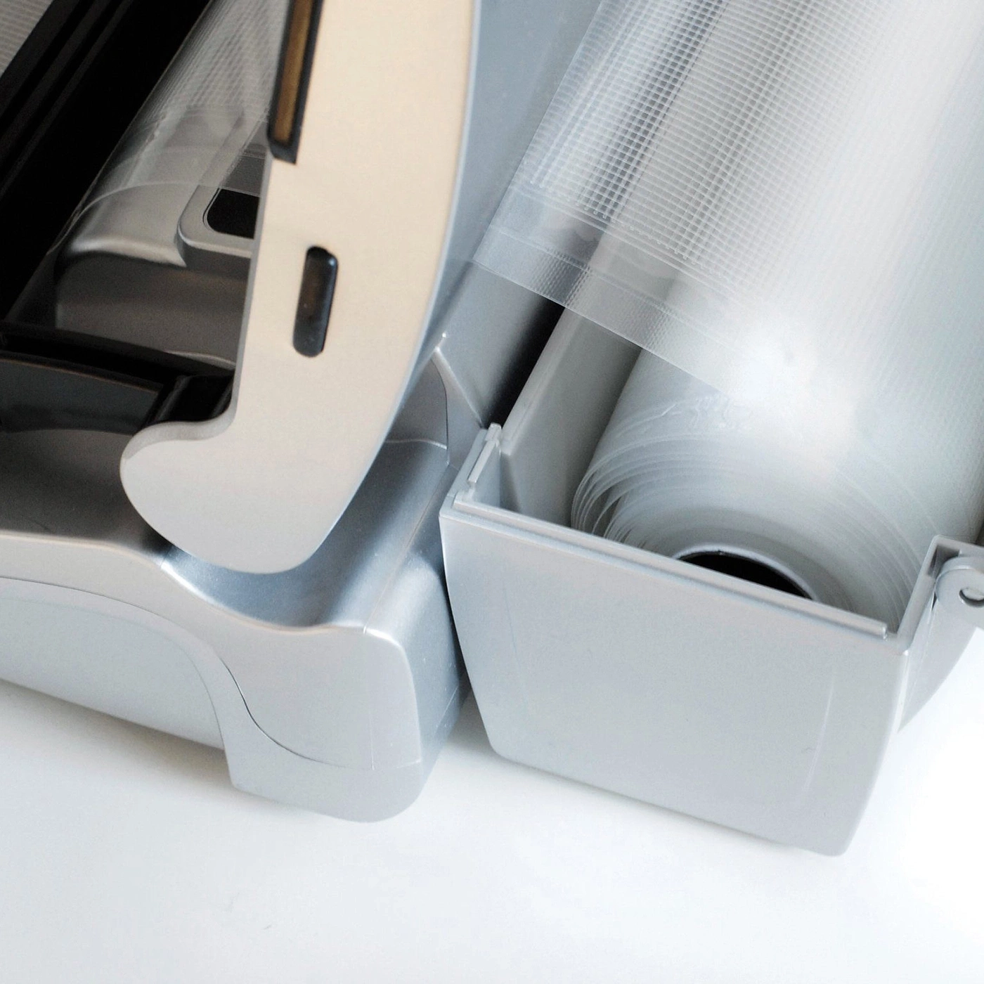 Close-up of a silver vacuum sealer with a roll of plastic film inside.