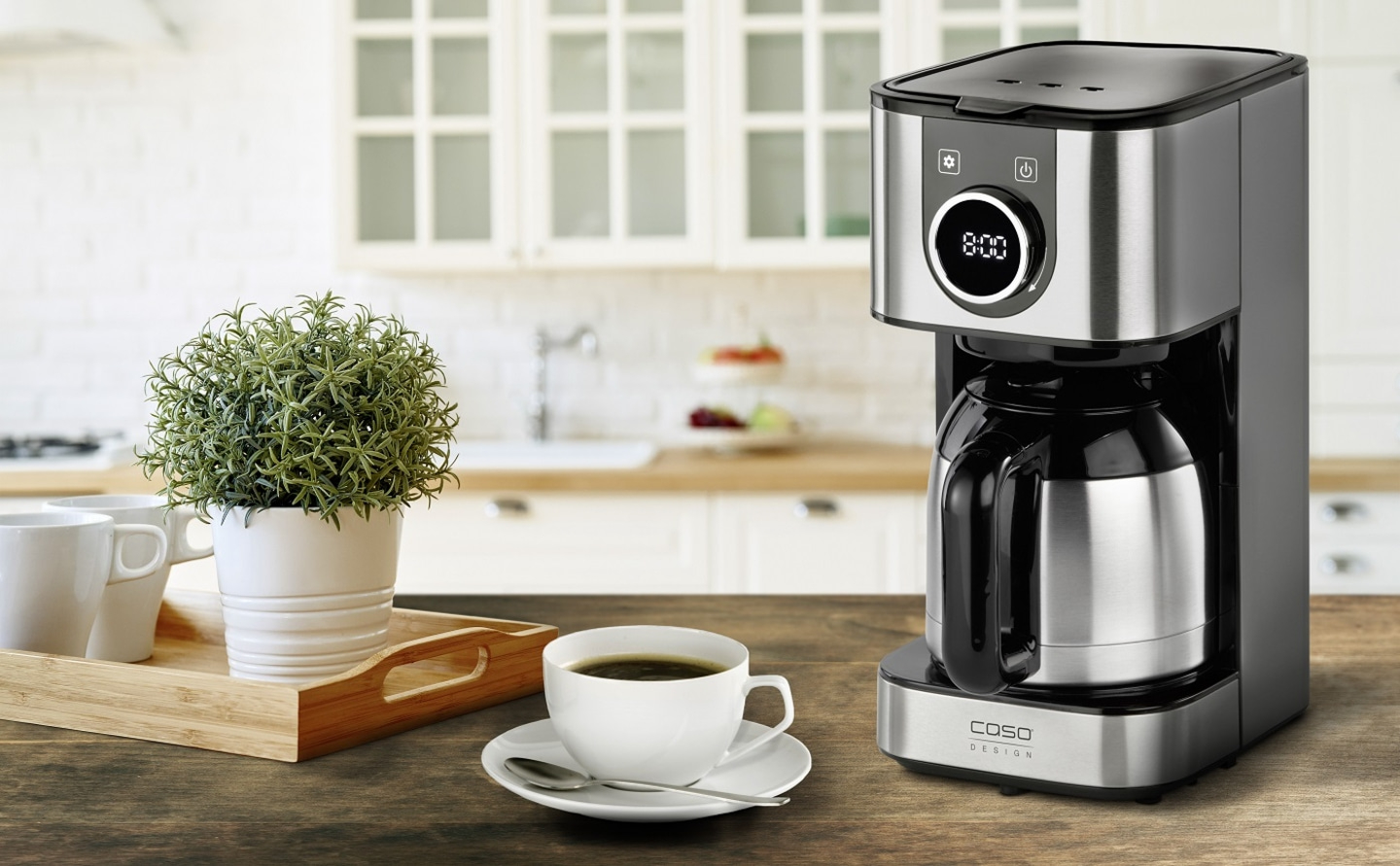 Kaffeemaschine mit Tasse, Tablett und Pflanze auf einem Holztisch in der Küche