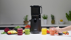 Black juicer with juice glasses and fruits on a white table