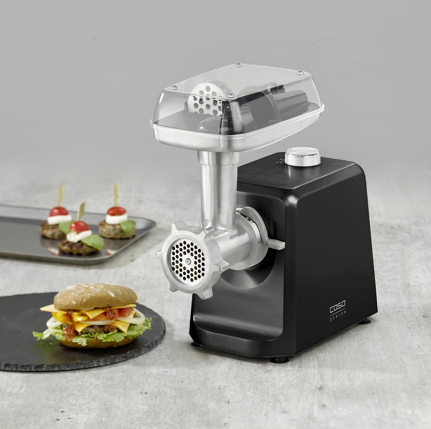 Fleischwolf mit Burger und Häppchen auf einem grauen Hintergrund