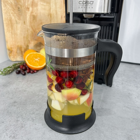 A glass with fruits and herbs, next to a coffee machine, close up shot.