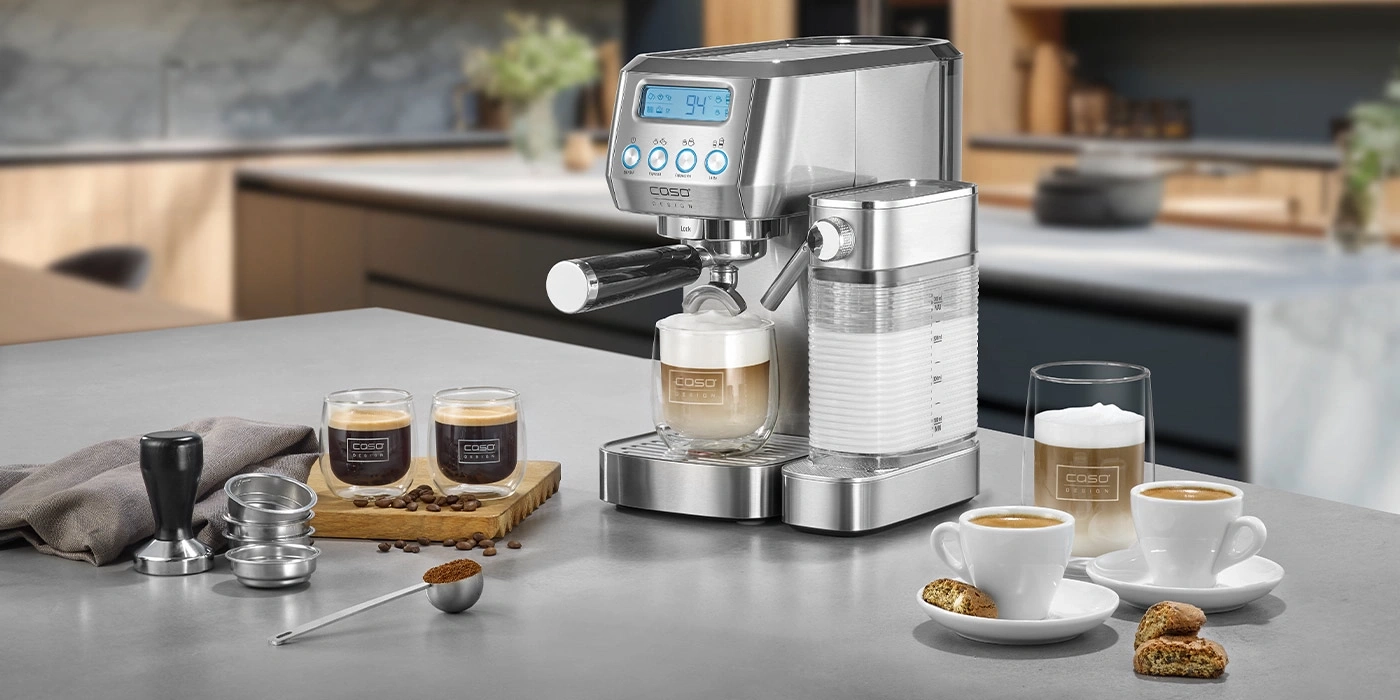 Kaffeemaschine mit Zubehör und Kaffeegetränken auf einer Arbeitsplatte in der Küche.