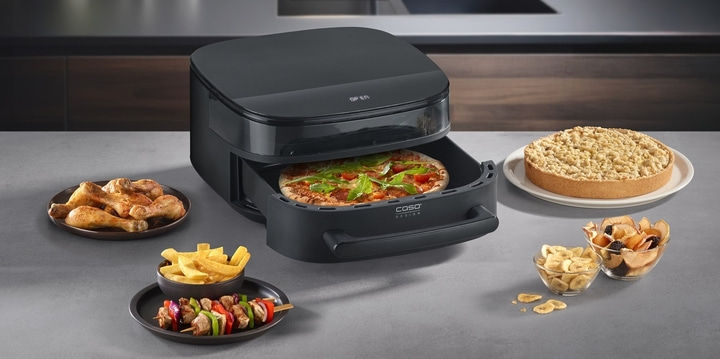 Eine Heißluftfritteuse mit Pizza, Hähnchenschenkeln, Pommes, Spießen, Kuchen und Trockenfrüchten.