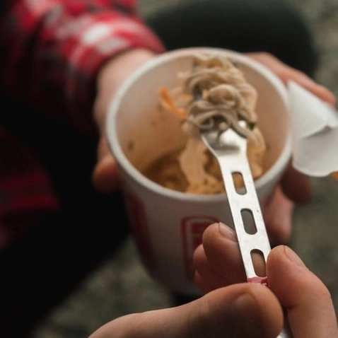Person eating noodles from a cup with a fork. Close-up shot of the food.