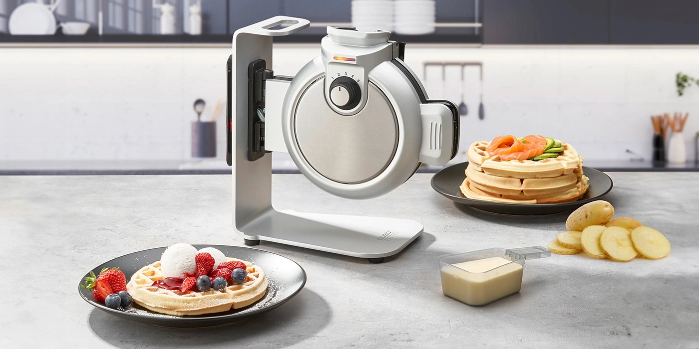 Waffeleisen mit Waffeln, Beeren, Lachs und Kartoffeln auf einem Tisch in der Küche.
