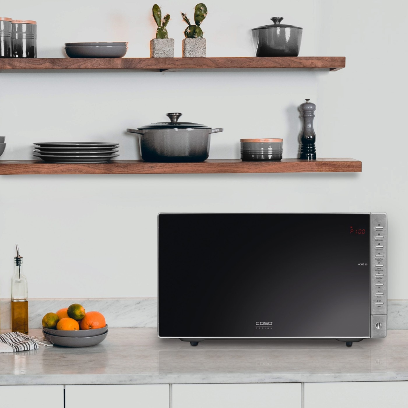 Microwave in kitchen with fruit, plates, and decor on shelves.