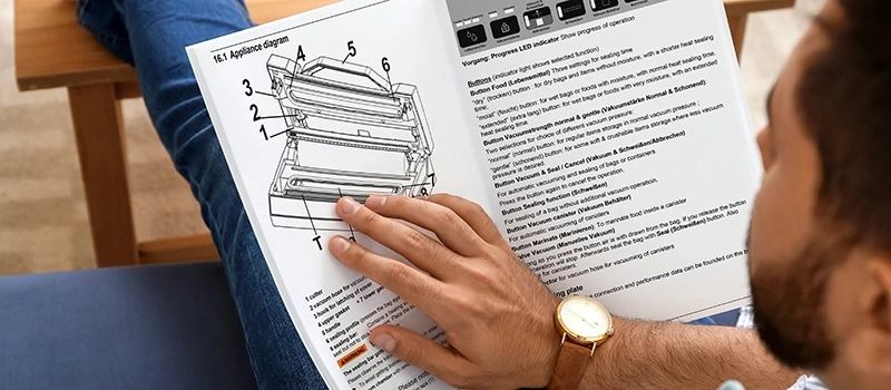 Mann liest Bedienungsanleitung für Vakuumiergerät. Diagramm, Knöpfe, Funktionen, Vakuum, Versiegelung, Lebensmittel.
