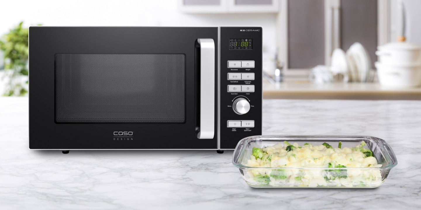 Black microwave with food in a glass dish on a marble surface in the kitchen.
