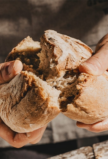Nahaufnahme von Händen, die ein Brot zerreißen, das in zwei Hälften geteilt wird