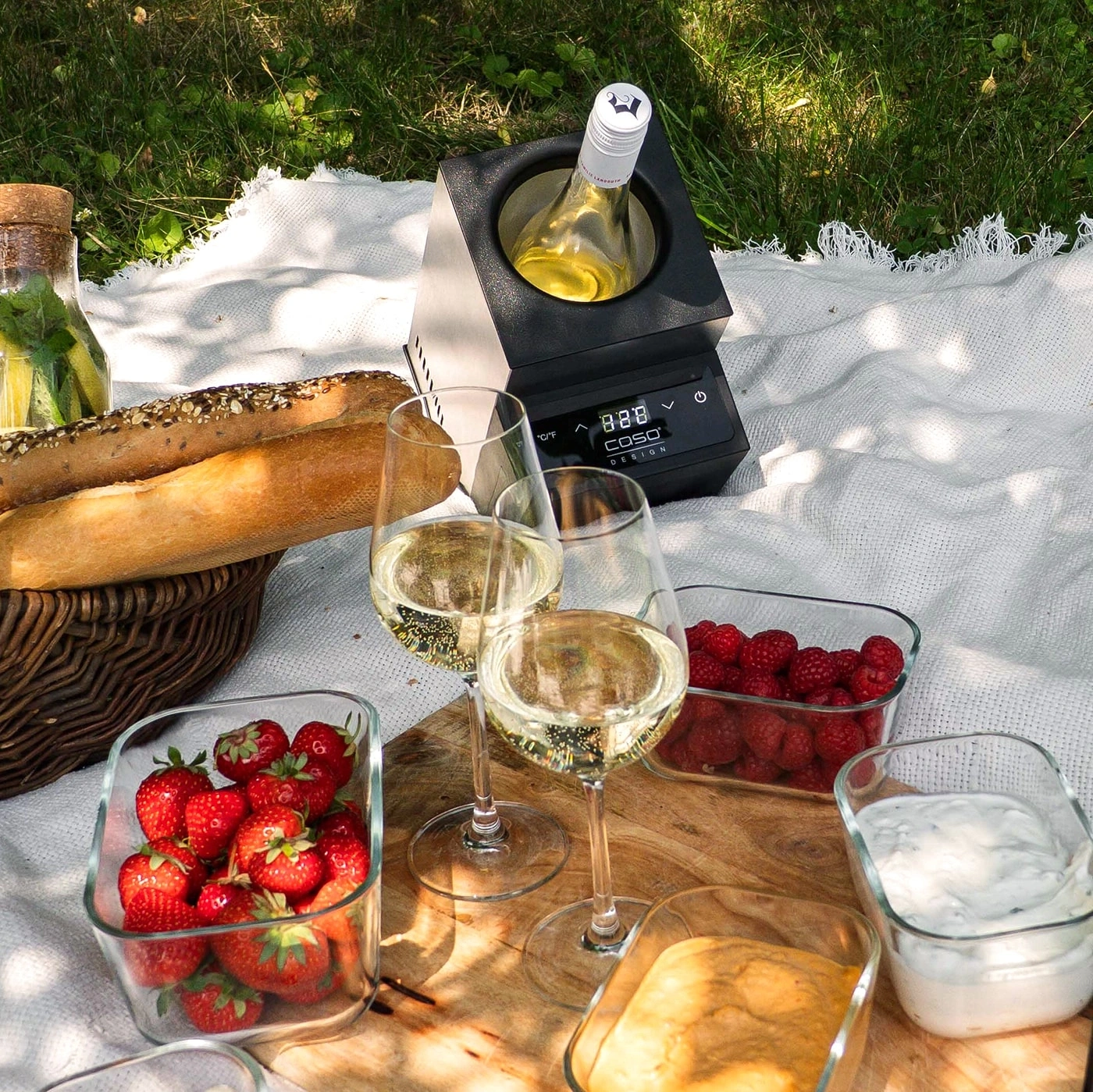 Picnic with wine, bread, berries, and dip on a blanket in the grass.