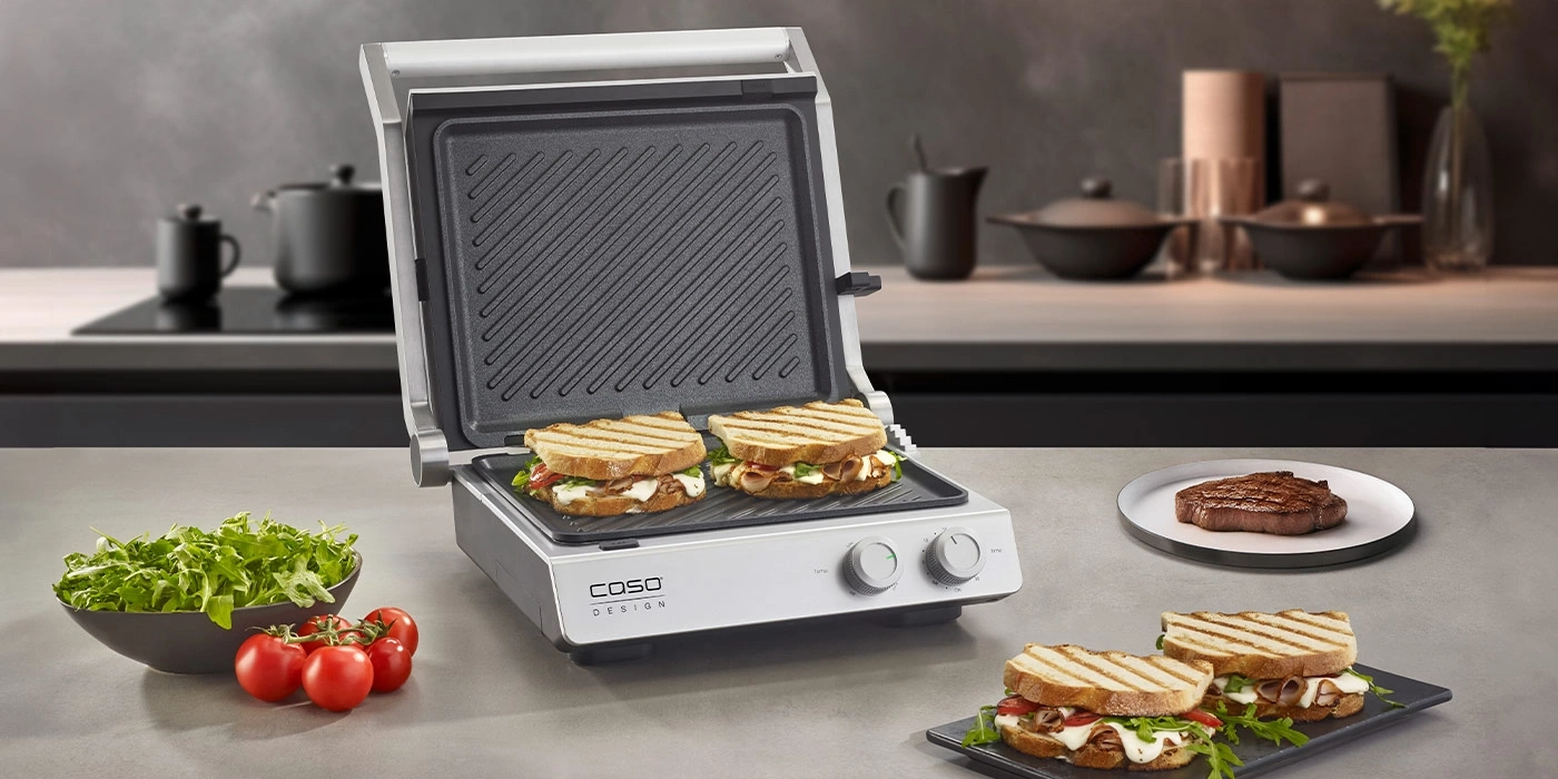 Sandwich-Grill mit Sandwiches, Steak, Tomaten und Salat auf dem Tisch.