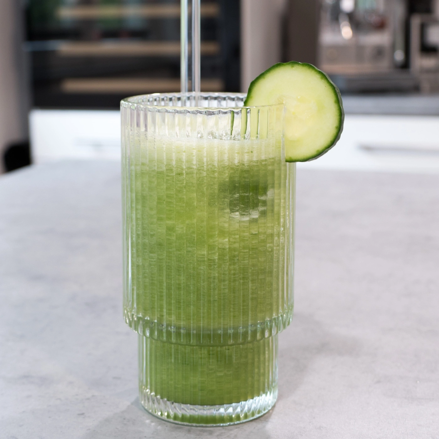 A green smoothie with a cucumber slice in a ribbed glass.