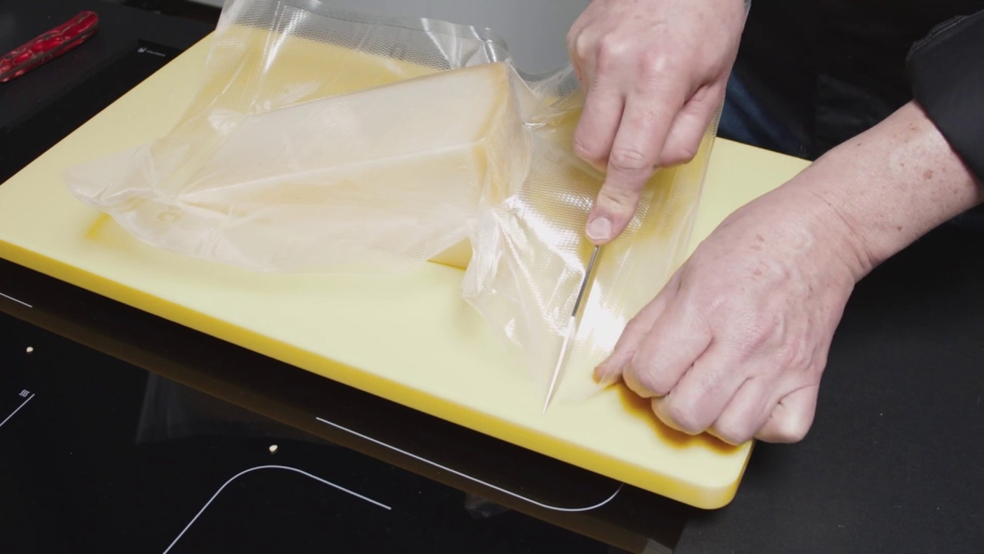 Person is cutting cheese out of the packaging on a yellow board with a knife.