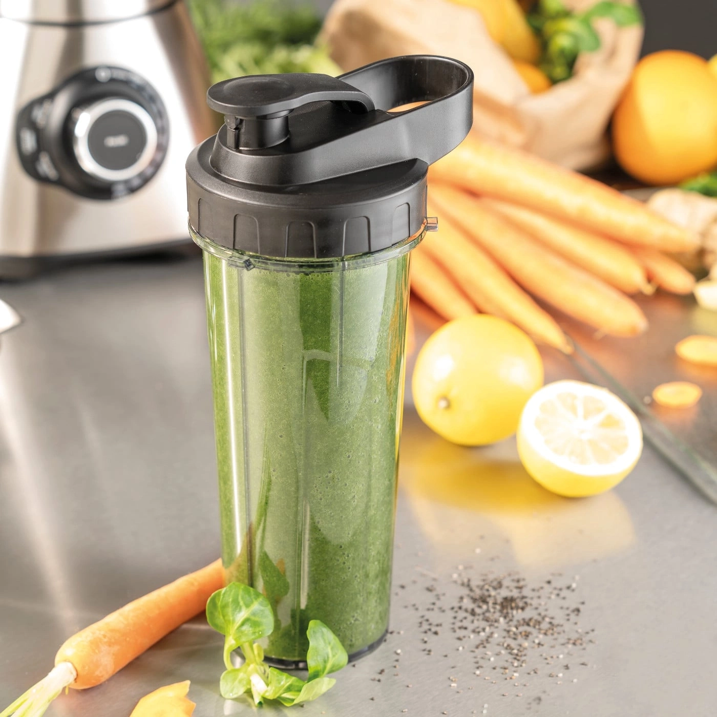Green smoothie in a shaker with carrots and lemon on the table.