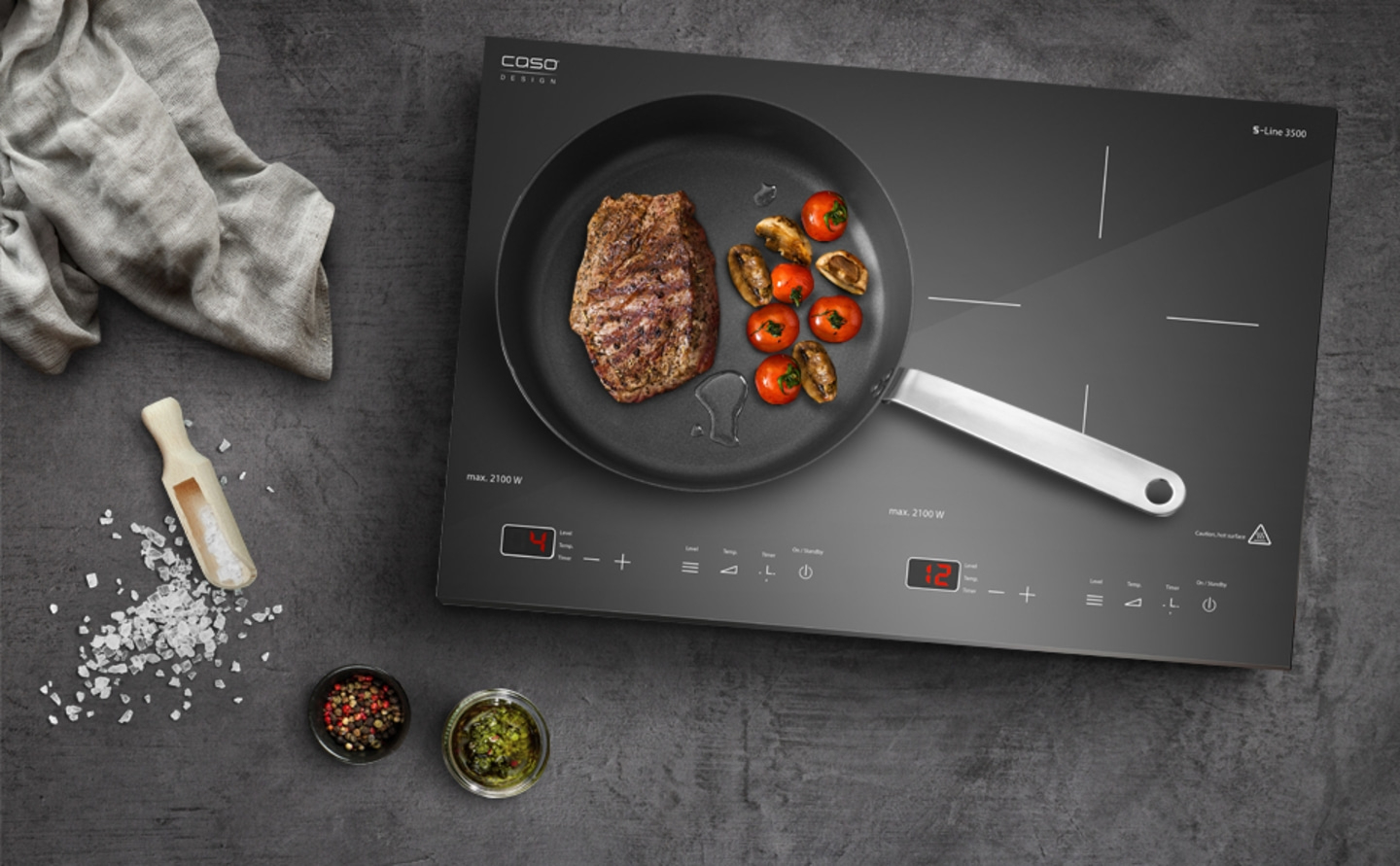Induction cooktop with steak, tomatoes, and mushrooms in a pan, with spices and salt.