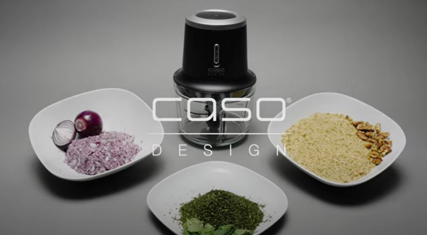Food processor with ingredients on plates, onions, nuts, and herbs.
