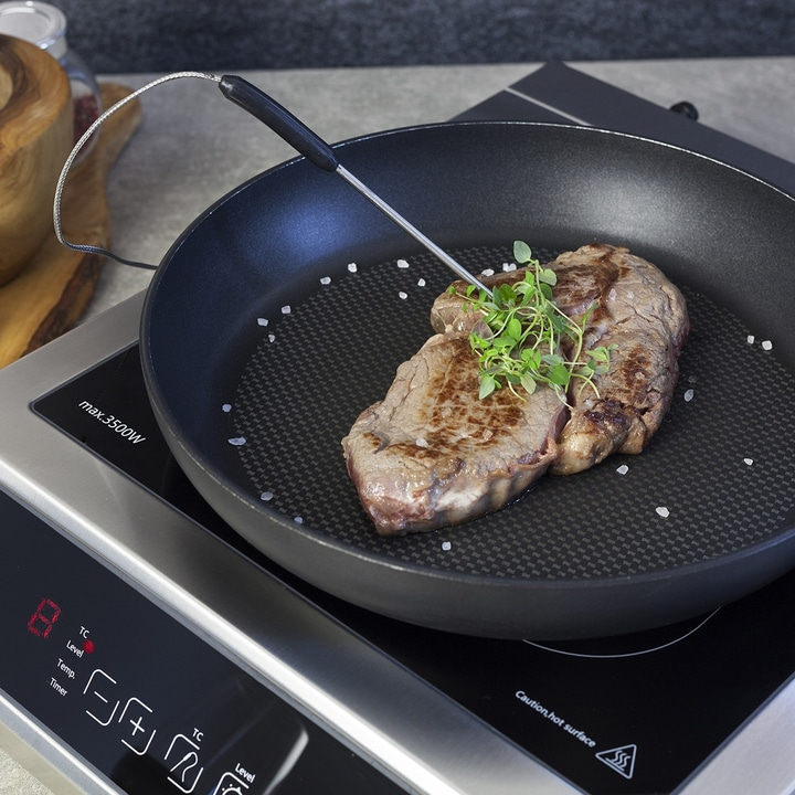 Gebratenes Steak in der Pfanne mit Kräutern und Thermometer auf Herdplatte