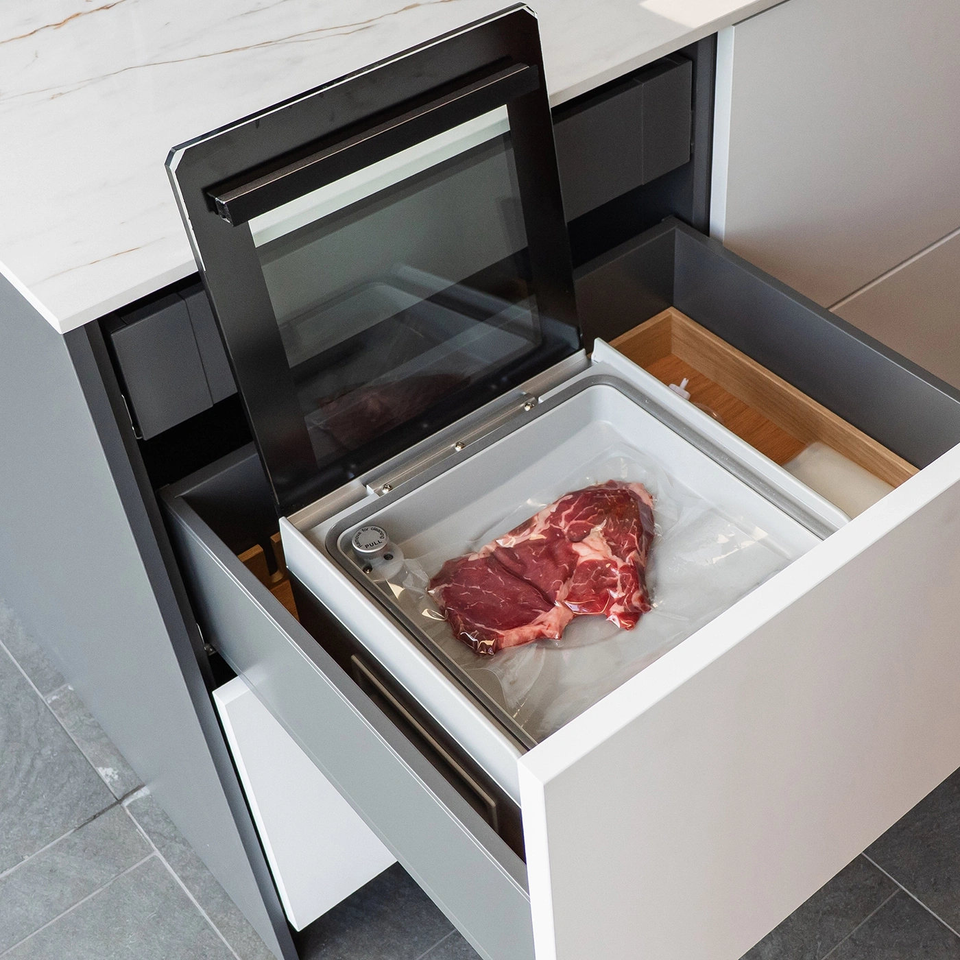 A raw beef steak in a vacuum sealer inside a kitchen drawer.