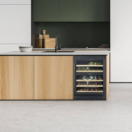 A modern kitchen with wooden cabinets and a built-in wine cooler filled with bottles.