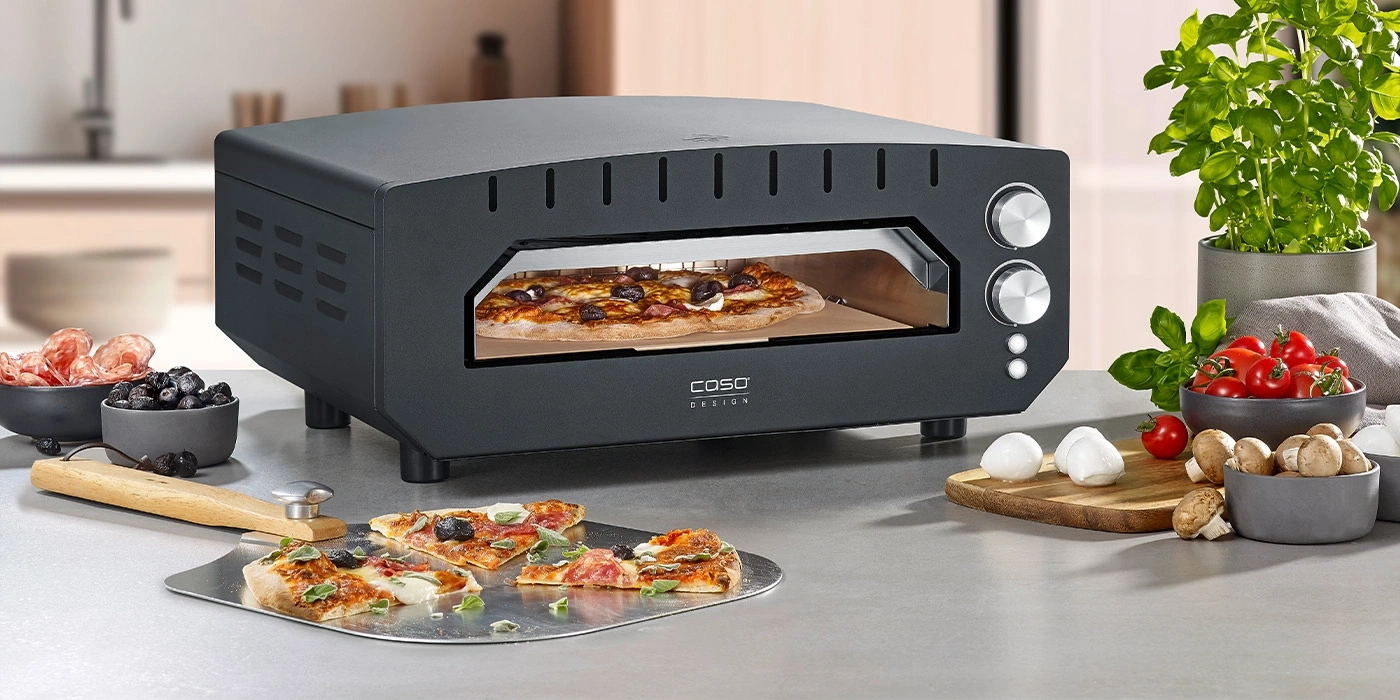 Pizza oven with pizza, ingredients, and pizza slices on a countertop.