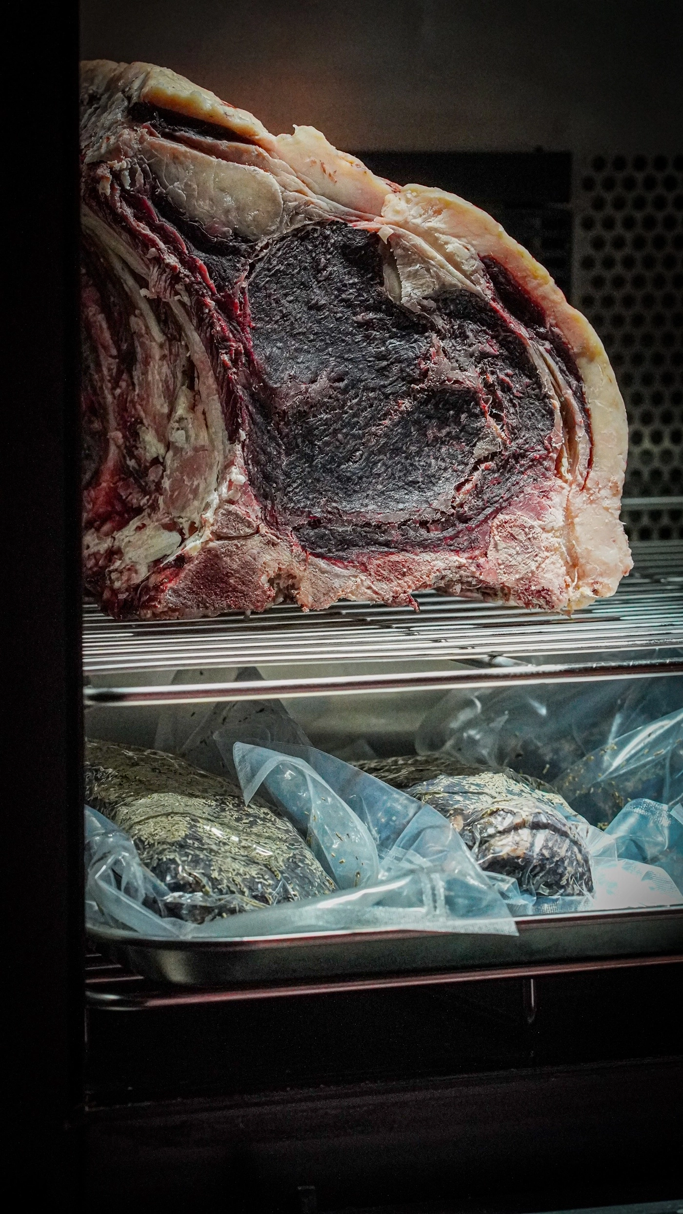 Large roast on a rack in a refrigerator. Vacuum-sealed meat underneath.