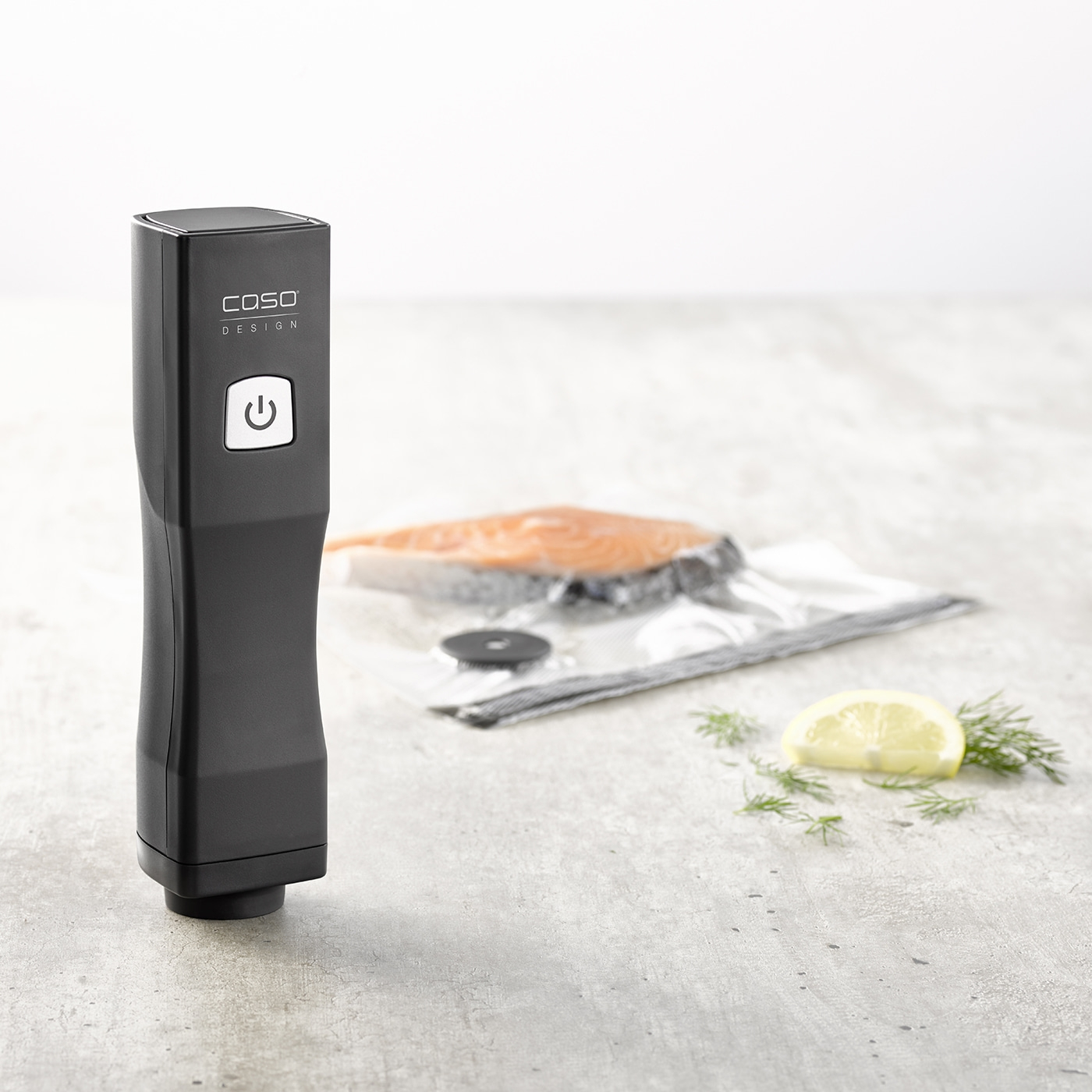 Black vacuum sealer with salmon, lemon, and dill on a gray background.