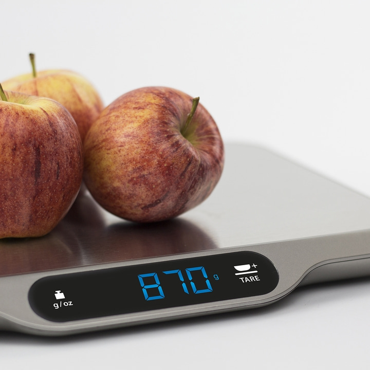 Apples on a scale showing 870 grams, set against a white backdrop.