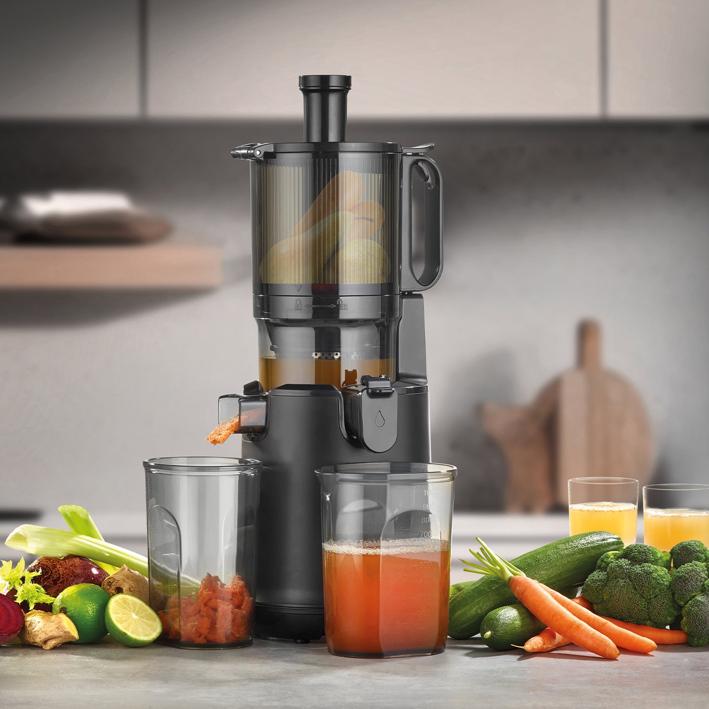 Juicer with vegetables and juice glasses on a kitchen countertop