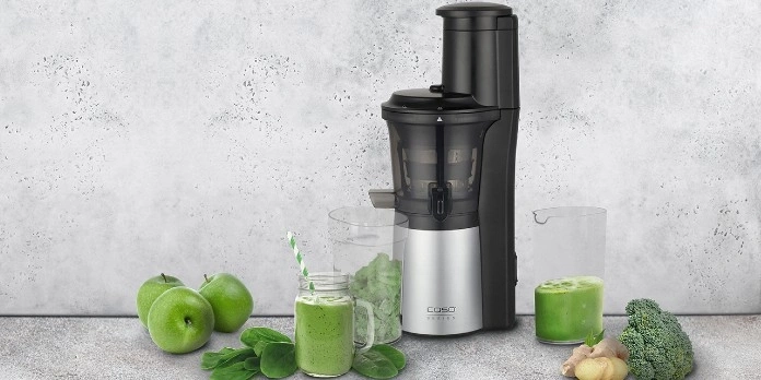 Ein Juicer mit Zutaten wie Äpfeln, Spinat und Ingwer für einen gesunden Saft.