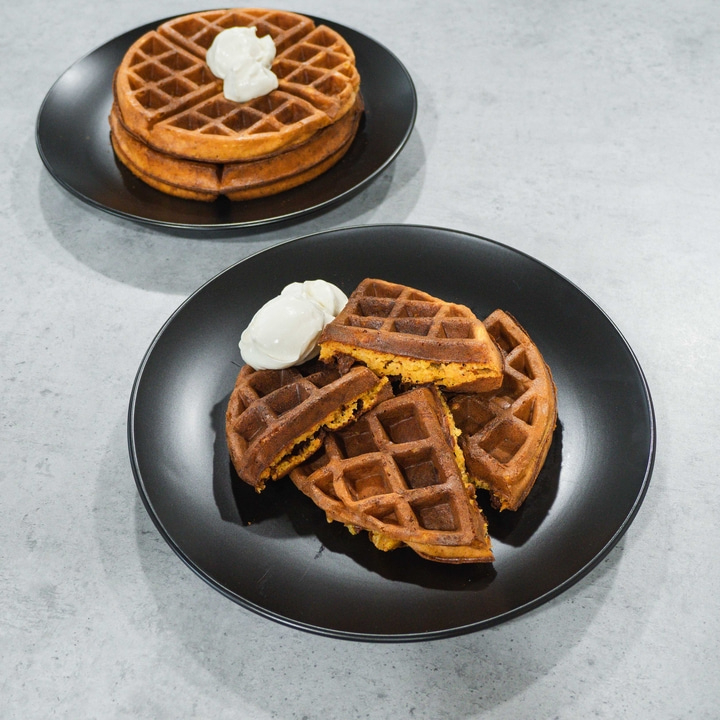 Waffeln auf schwarzen Tellern mit Sahne, auf grauem Untergrund, Nahaufnahme