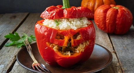 Ein roter Paprika, der mit Reis gefüllt und zu Halloween dekoriert wurde, steht auf einem Teller.