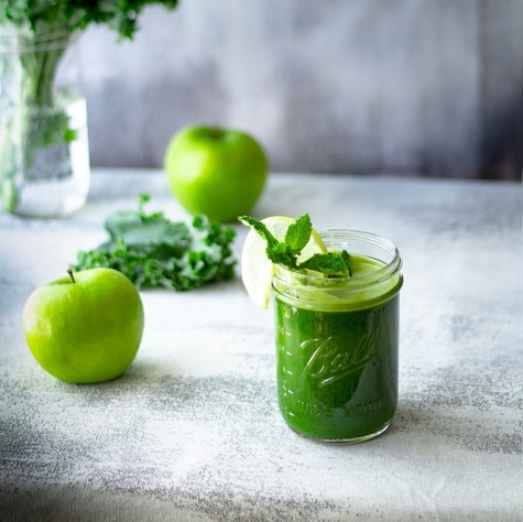 Grüner Smoothie mit Äpfeln, Zitrone und Minze in einem Glas auf einem Tisch.