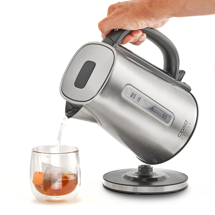 Person pouring hot water from a kettle into a glass with a tea bag.