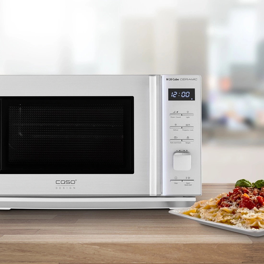 Microwave with pasta on a table. Caso Design, M 20 Cube Ceramic, 12:00 time display.