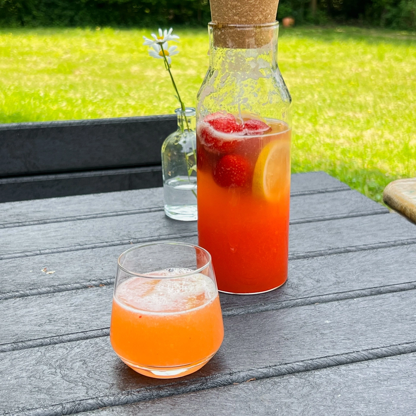 Ein Glas und eine Karaffe mit Getränk auf einem Tisch im Freien.