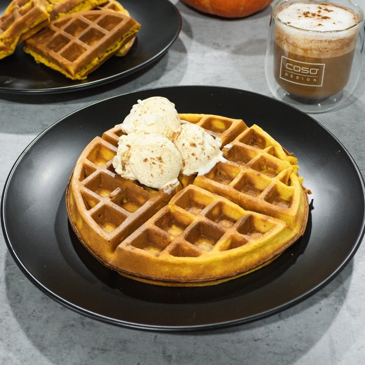 Waffle with ice cream on a black plate, drink beside it, delicious food.