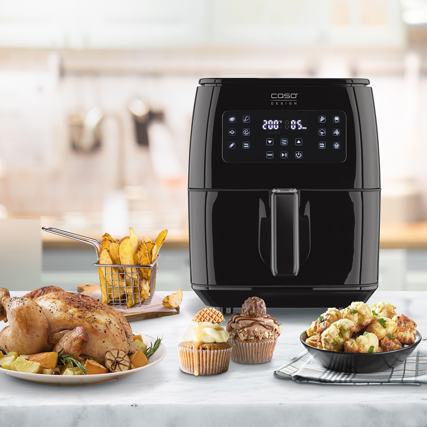 Black air fryer with food, chicken, fries, cupcakes and cauliflower
