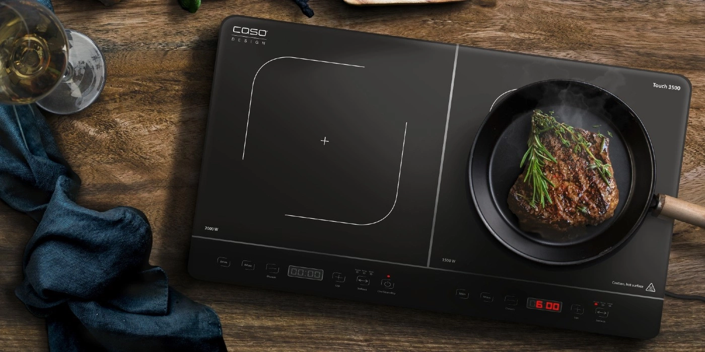 Induction cooktop with steak in pan on a wooden table