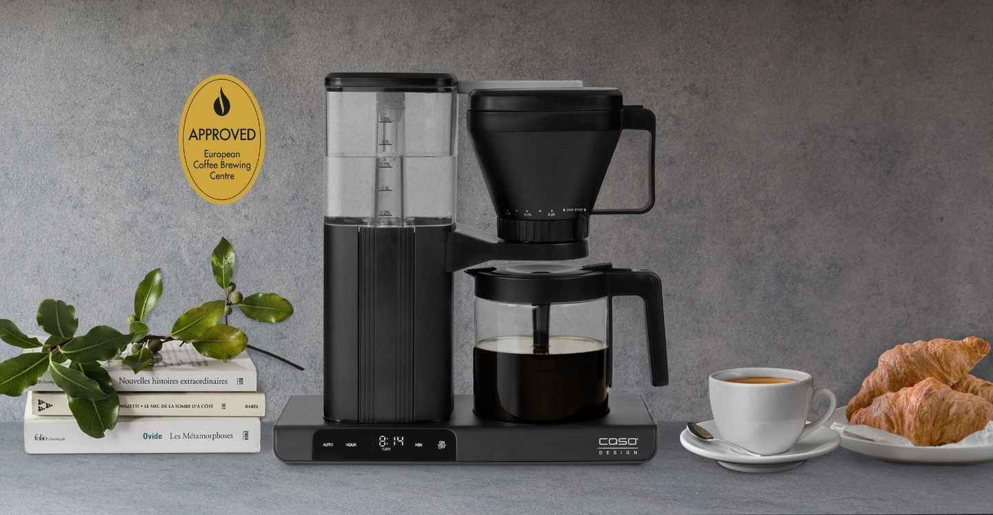 Kaffeemaschine mit Kaffee, Tasse, Croissants und Büchern auf einem Tisch.