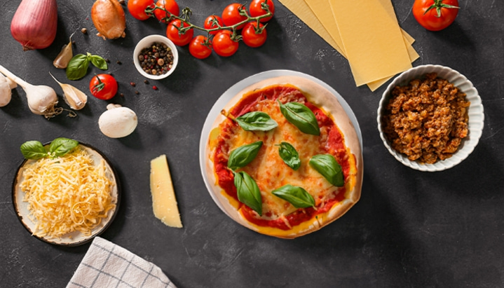 Pizza mit Zutaten wie Tomaten, Käse, Basilikum und Hackfleisch auf dunklem Hintergrund.