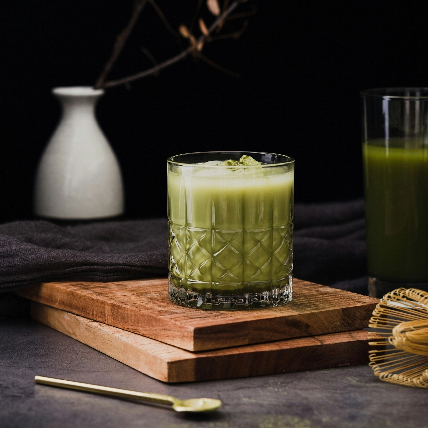 Matcha drink in a glass on a wooden board, with accessories and background.