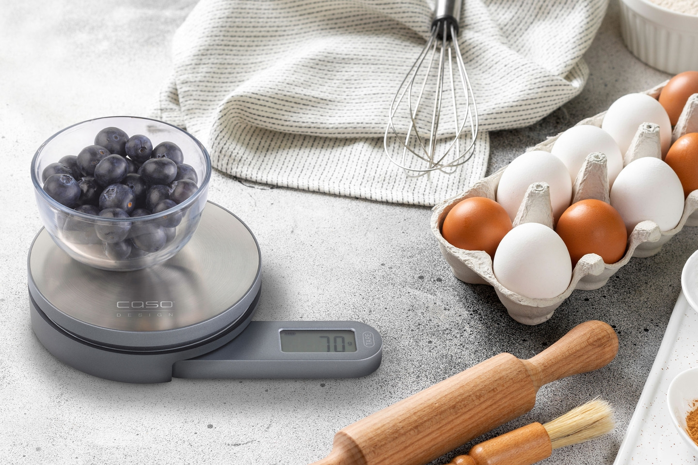 Blueberries on a scale, eggs, whisk, baking utensils on a gray background