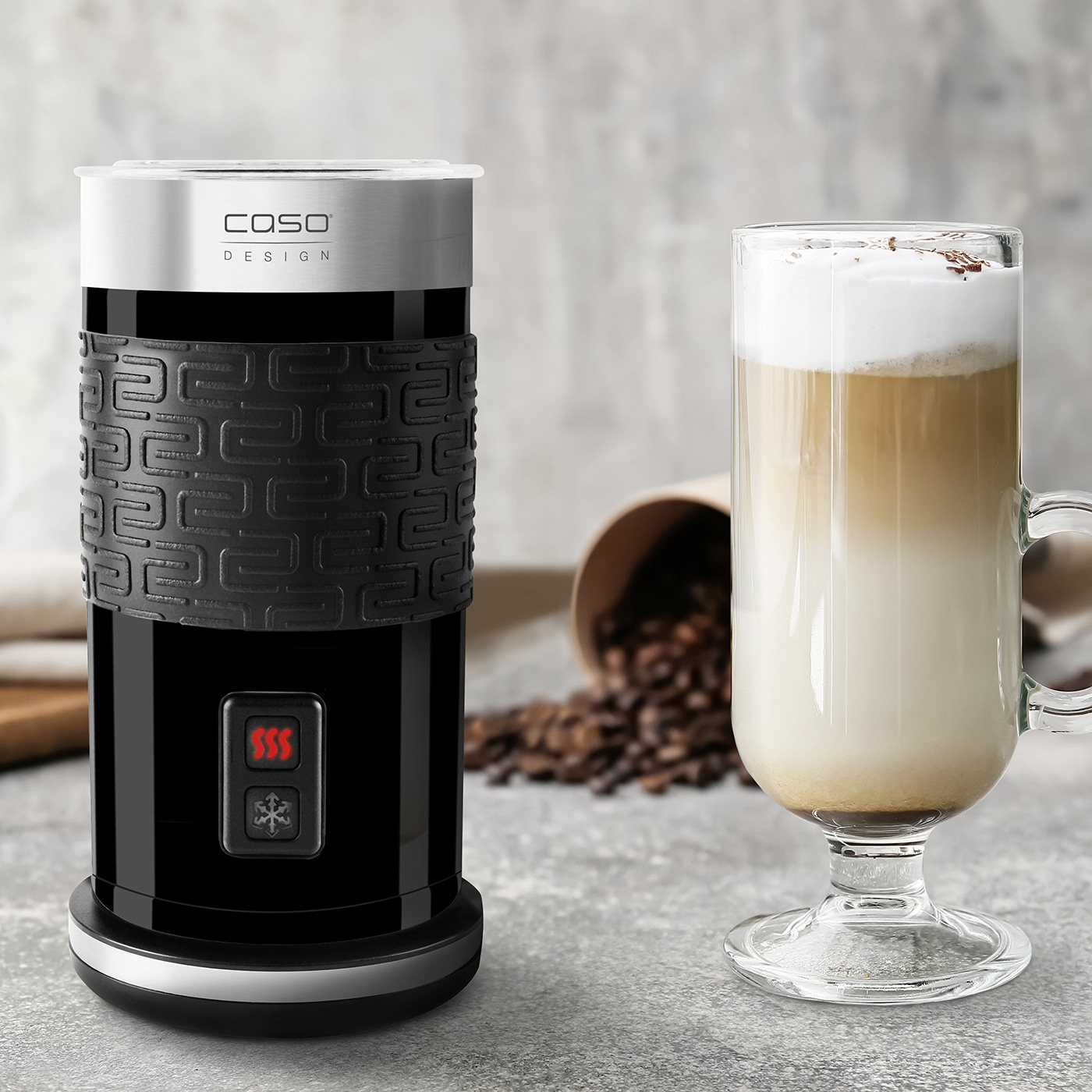 Milk frother and latte macchiato with coffee beans on a gray background