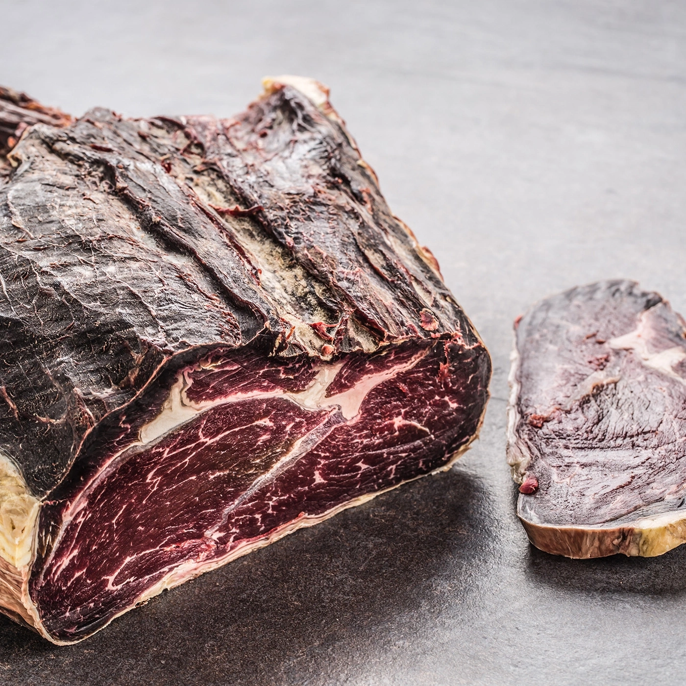 Two pieces of dry-aged beef on a dark stone surface