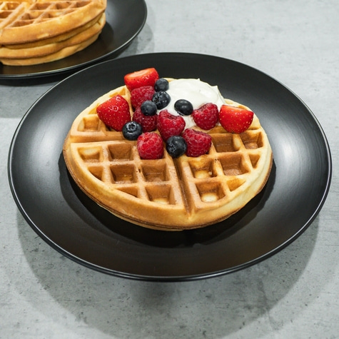Waffle with berries and cream on a black plate, close-up shot