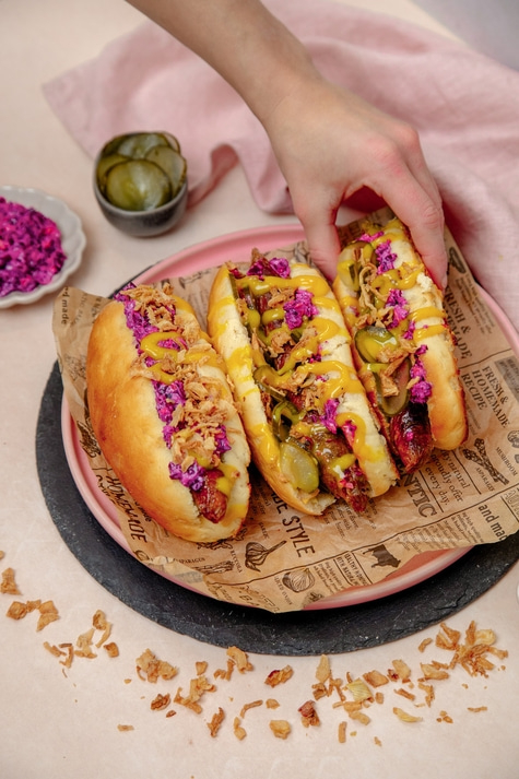 Drei Hotdogs auf einem Teller mit Toppings und Beilagen, Nahaufnahme.