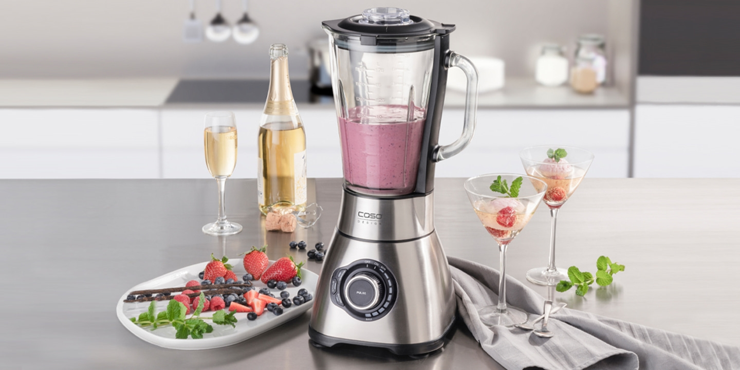 Blender with fruits, champagne, and cocktails on a countertop setting.