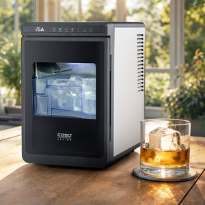 Ein schlanke schwarze Eismaschine steht auf einem Holztisch neben einem Whiskeyglas mit einem großen Eiswürfel.